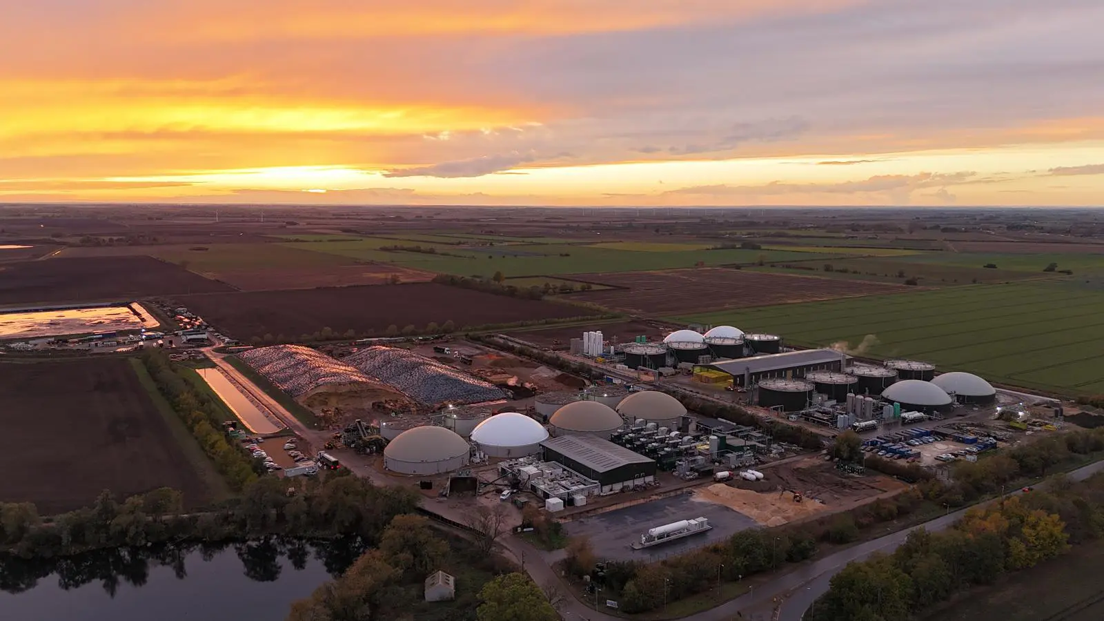 Aerial view showcasing a renewable gas refuelling station, including large storage domes, and surrounding farmland during sunset, highlighting the importance of Bio-LNG and Bio-CNG for UK logistics fleets.