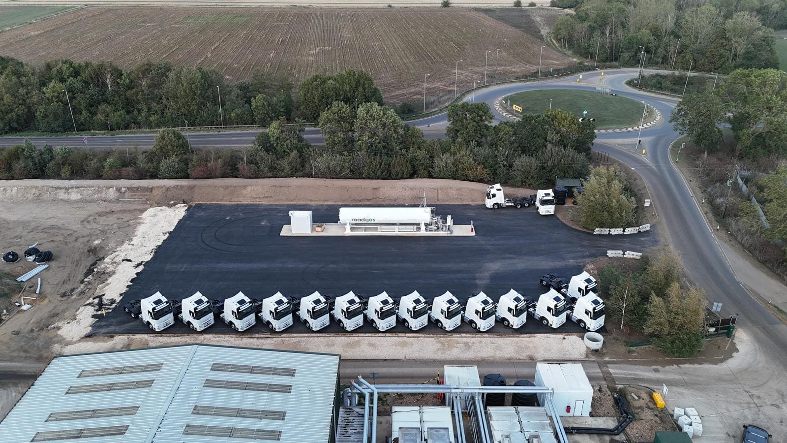 Aerial view of a Roadgas refuelling station featuring multiple Bio-LNG trucks parked in a line, surrounded by greenery and road infrastructure.